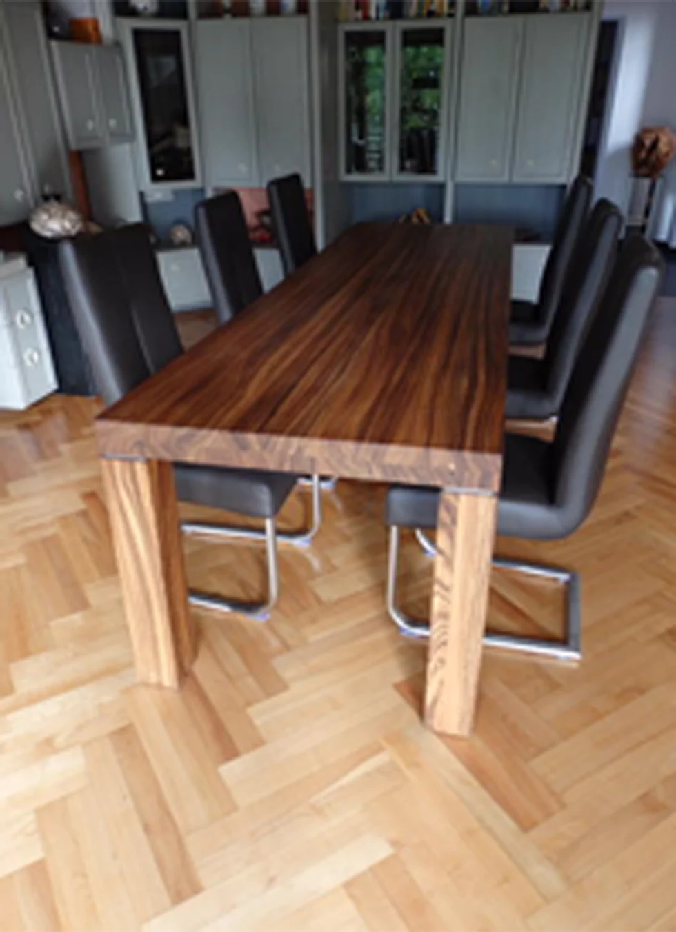 Ein brauner Esszimmertisch steht vor einem mintgrünen Schrank und um den Tisch herum stehen sechs schwarze Stühle.