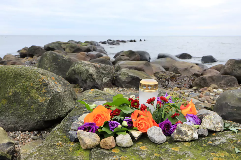 Begräbnisdekoration mit Kerze mit Blumenschmuck auf Steinen an einem Strand