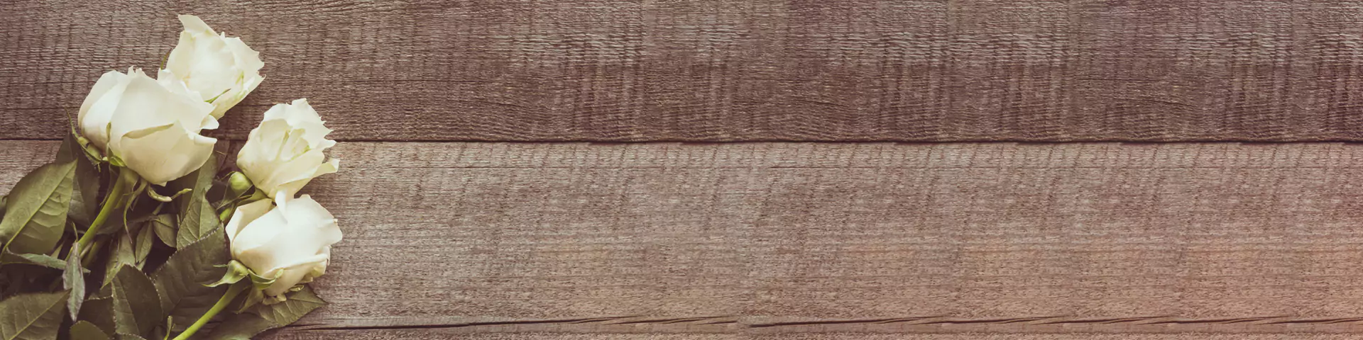 5 weiße Rosen liegen auf einer Holzplatte